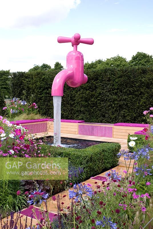 Path with pink glass tiles leading to a seating area next to a pond with a pink tap water feature, planting include Agapanthus 'Dr Brouwer', Cosmos, Geranium psilostemon and Knautia macedonica - 'A Matter of Urgency', Silver Gilt medal winner - RHS Hampton Court Flower Show 2010 