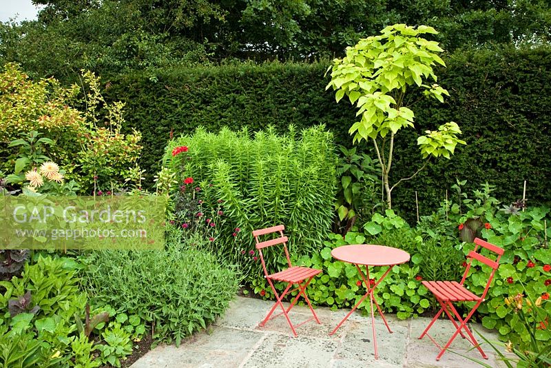 Hot border with colour co-ordinated furniture - Wilkins Pleck NGS, Whitmore, Staffordshire, UK. July 