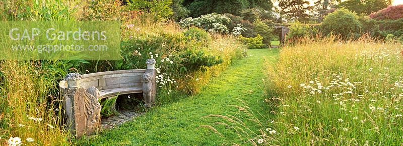 A stone seat beside a grass path in the wildflower meadow at Ince Castle, Cornwall
