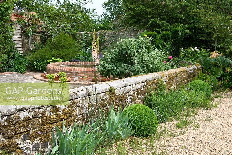 Front garden with stone wall and gravel path with Eremurus and Buxus - Box balls. Sandhill Farm House, Hampshire.