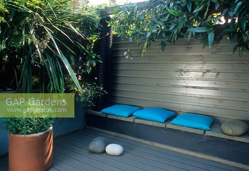 Small town courtyard garden with decking, tropical style planting and built in bench. Cordyline australis in terracotta pot, Clematis armandii growing on fence. Alistair Davidson, Worcester, UK