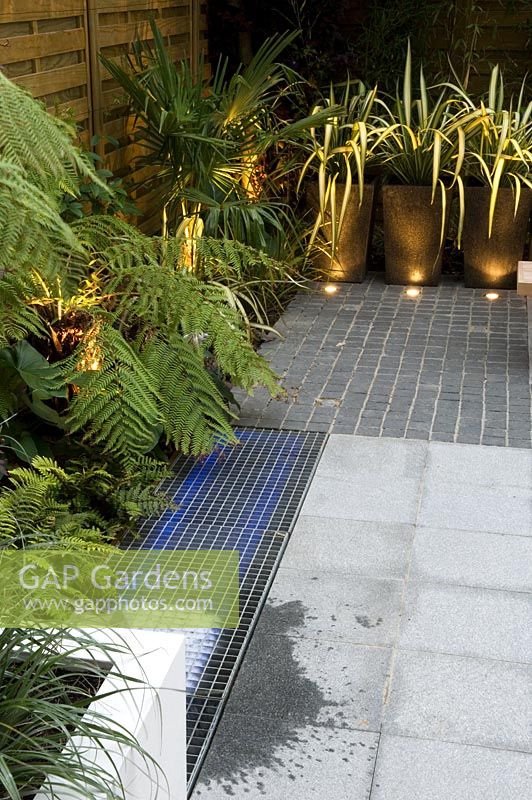 Small urban courtyard garden with Phormium in containers and uplighting