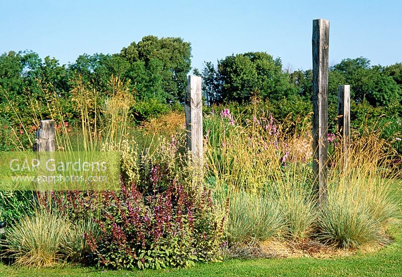 Wooden sculptures in a dry coastal garden with grasses and perennials