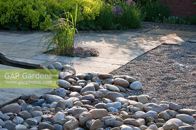 Flagstone paved area leading to a 'beach zone' with pebbles, softened up by interplanted grasses and Thymus