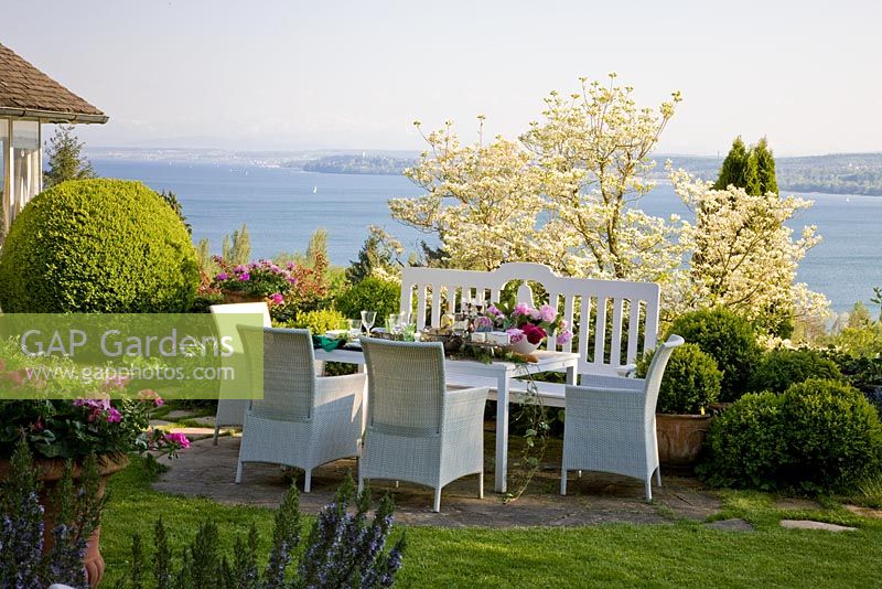 Table and chairs, planting of Buxus, Cornus, Pelargonium and Rosmarinus, overlooking the lake of Constance, Germany 