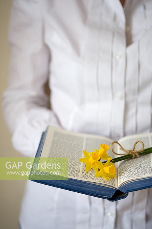 Woman wearing a white shirt, holding an open book with a small bunch of daffodils 