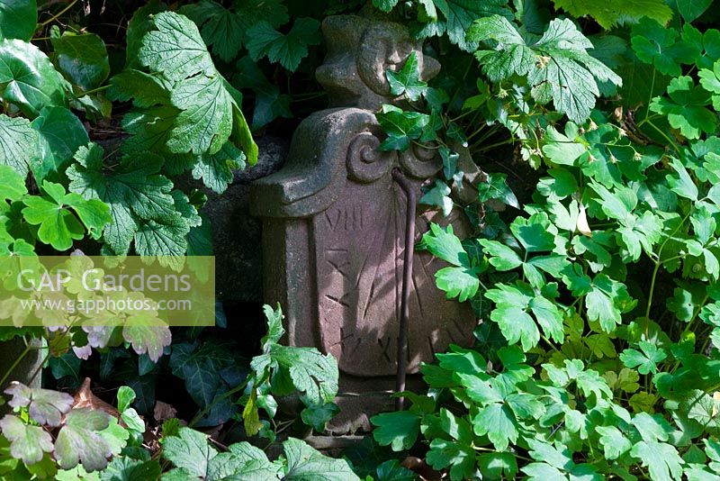 Antique stone sundial half hidden under leaves of Aquilegia and Waldsteinia geoides - The Manor House, Germany
