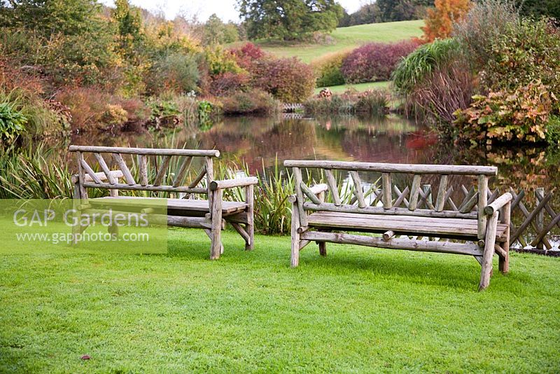 Wooden benches overlooking landscaped lake in autumn - Lady Farm, Somerset