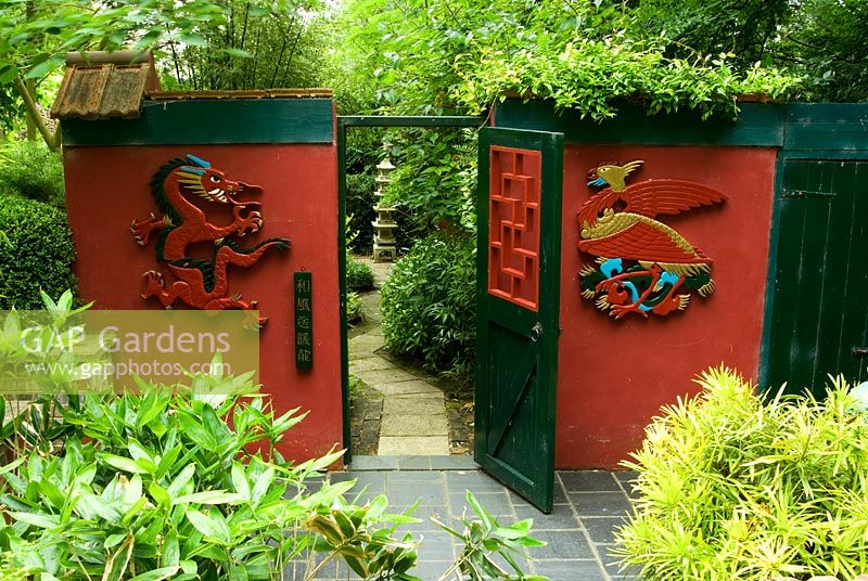 Three-Friends-of-Winter garden has a winter flowering plum, Prunus mume, at its centre and Sasa veitchii - Bamboo. Hand carved Phoenix and dragon flank gate into Red Wall Garden. Beggars Knoll, Newtown, Westbury, Wiltshire, UK