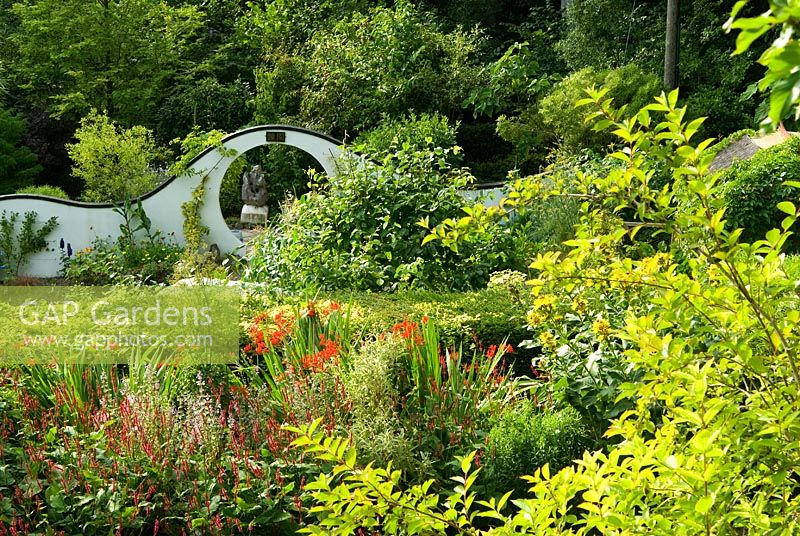 View from Wildly-Cheering Pavilion giving views over the herbaceous border and into the kitchen garden backed by undulating white wall containing moon gate. Beggars Knoll, Newtown, Westbury, Wiltshire, UK