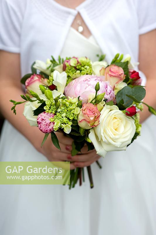 Girl in a white dress holding a bridesmaid bouquet of roses and peony