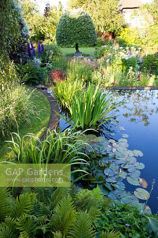 Summer garden, large formal pond surrounded by informal planting - The Corner House, Wiltshire.