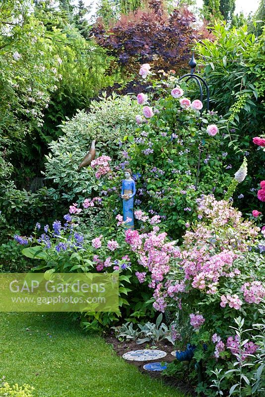 Sculpture of woman and other ceramic objects next to border of Buxus - Box, and Rosa 'Ballerina' 'Eden Rose'