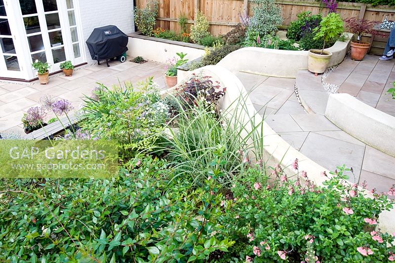 Elevated view of sloping small modern garden with white painted walls, terrace and tiered planting.