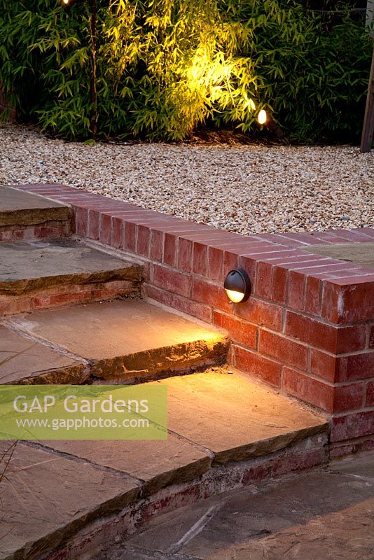 Brick edged stone steps and gravel patio lit up at night. Fargesia nitida - Bamboo