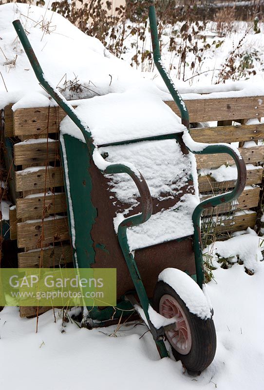 Wheelbarrow covered in snow next to compost heap in winter