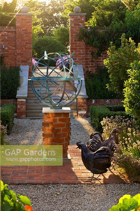 Metal armillary sundial and hen statues on red brick patio, Oxfordshire 
