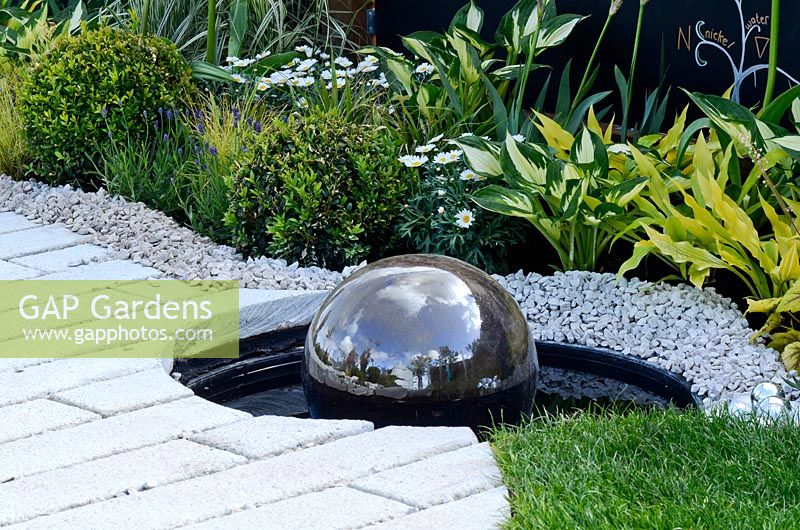Water feature with reflecting ball, surrounded by gravel and white bricks.  