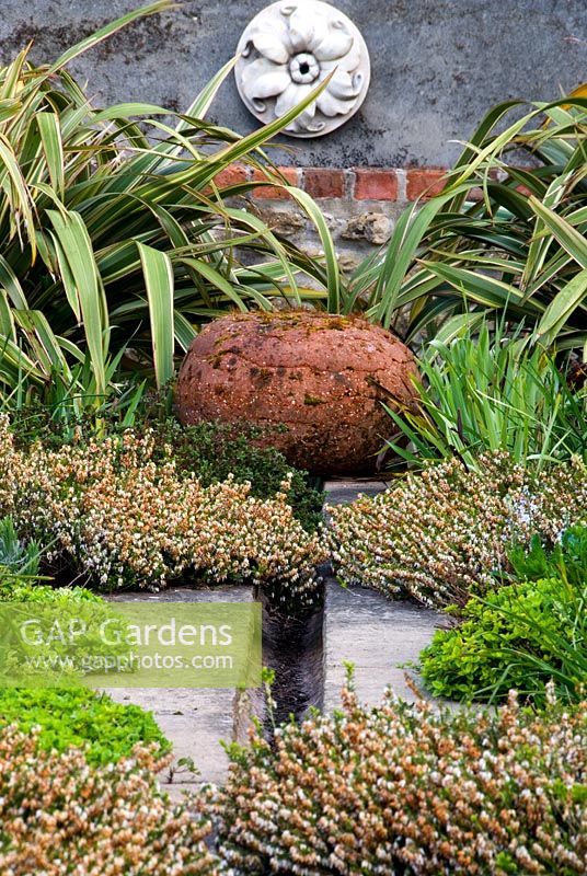 Rill garden with terracotta spheres and plants including Phormium tenax, Potentilla fruticosa 'Primrose Beauty', Erica carnea 'Springwood White', Dorset
