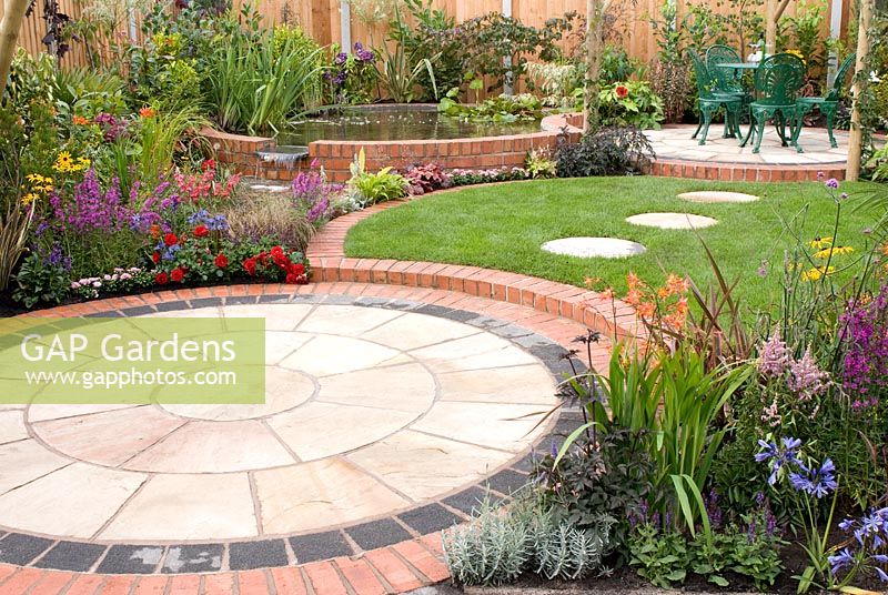 Small back garden with colourful borders, circular patios with seating, lawn with stepping stones and raised brick pool by Mook Garden Design - Southport Flower Show 2011