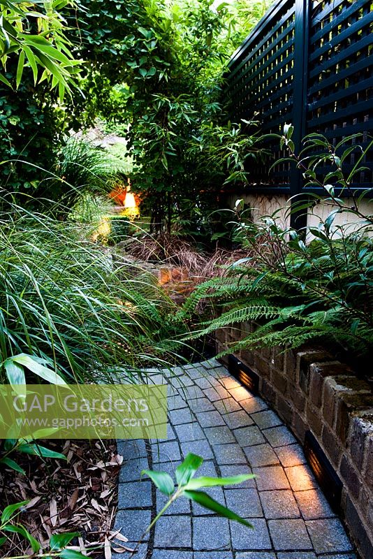 Pathway through illuminated raised beds in secluded suburban garden at dusk 