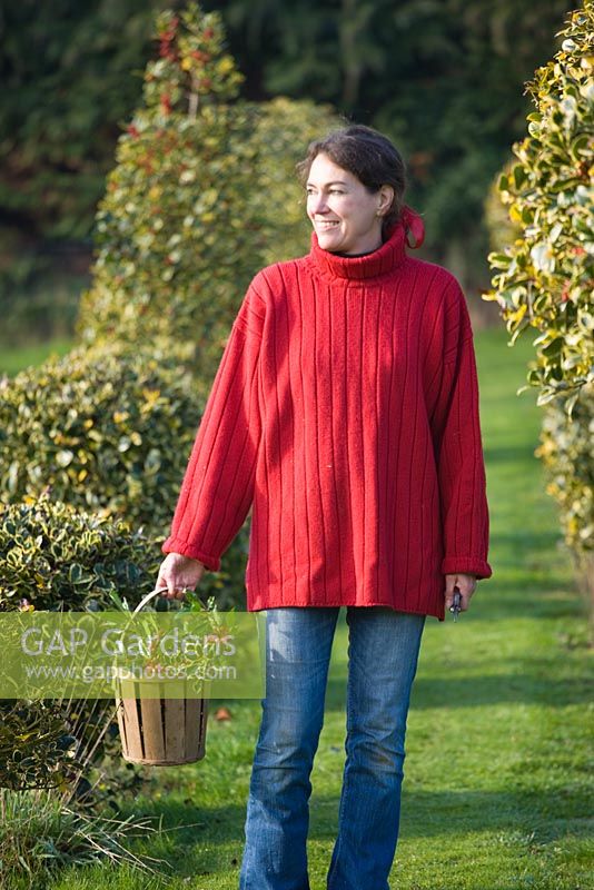 Woman in red jumper carrying wooden basket of holly