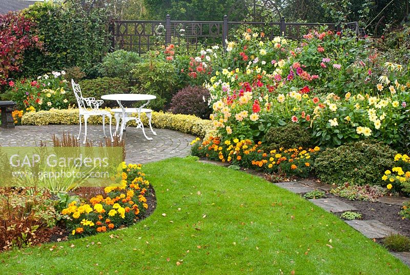 Late summer garden with path leading to circular cobble sett patio and seating, and colourful mixed borders with Azalea, Astilbe and summer bedding Dahlia and Tagetes