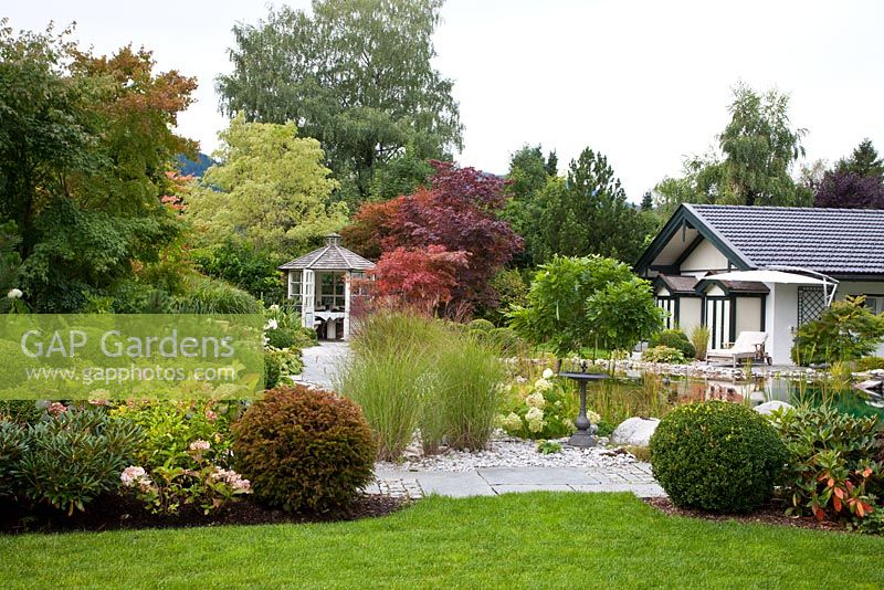 German garden with pavilion, garden pond, grasses and Box spheres. Plants include - Acer negundo 'Variegatum', Acer palmatum, Acer saccharinum, Betula pendula, Buxus, Hydrangea, Miscanthus sinensis, Pinus, Rhododendron, Taxus baccata and Wisteria