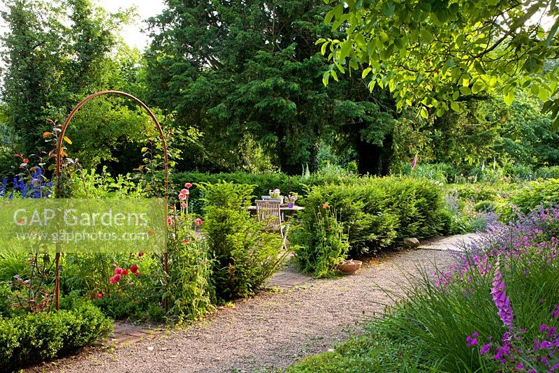 A Yew hedge separating a rest area from the gravel path, planting includes - Geranium 'Sirak', Juglans regia, Nepeta 'Six Hills Giant' Faassenii-Gruppe, Papaver, Pennisetum alopecuroides 'Hameln' and Taxus baccata - Jens Tippel