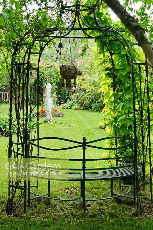 Wrought iron arbour with seat and flying pig ornament suspended on chain -  The Rowans, Threapwood, Cheshire.