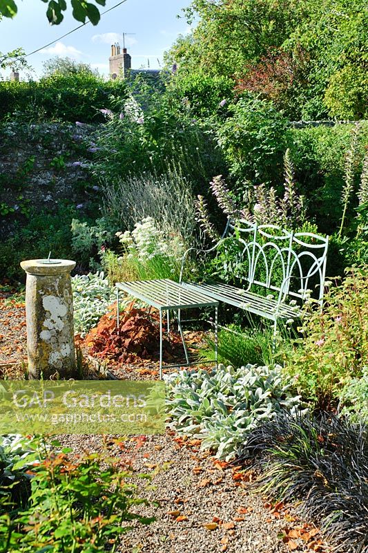 Formal garden with blue painted wrought iron bench, old sundial, gravel paths, roses and herbaceous perennials - Barnwells, Cerne Abbas, Dorset.
