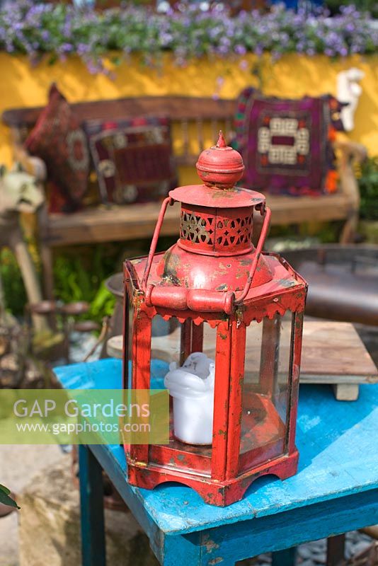 Lantern on table, wooden bench with decorative pillows in background - RHS Chelsea Flower Show 2011