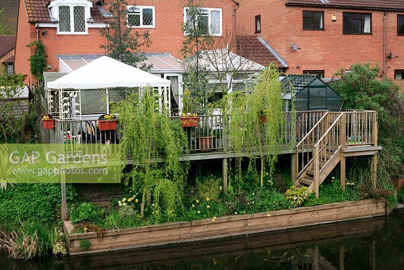 Riverside garden with suspended timber deck providing a level area for a greenhouse and tented pavilion. Weeping willows provide some privacy