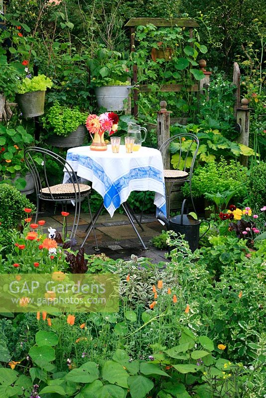 Small seating area with table and chairs laid with drinks as the centrepiece of a small ornamental kitchen garden, built largely from recycled materials and planted with vegetables, herbs, flowers for cutting and as companion plants to deter pests and attract beneficial insects