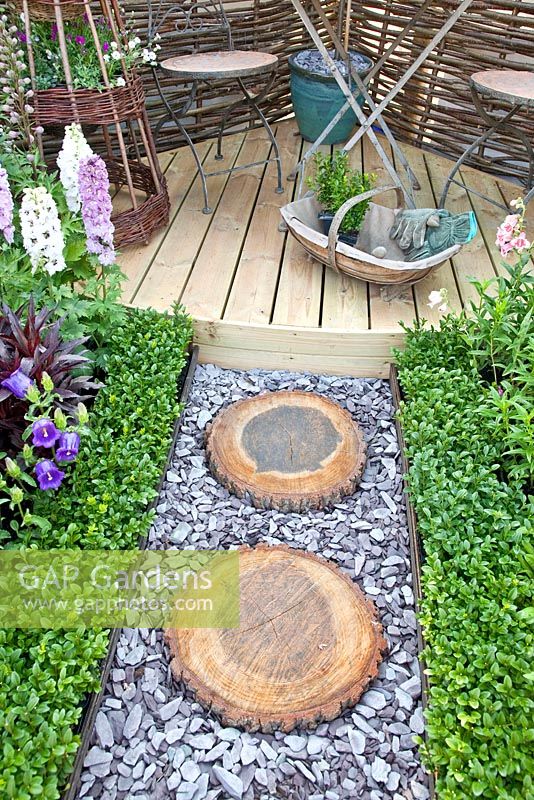 Corner of small garden with path of slate chippings and stepping stones made from sawn logs