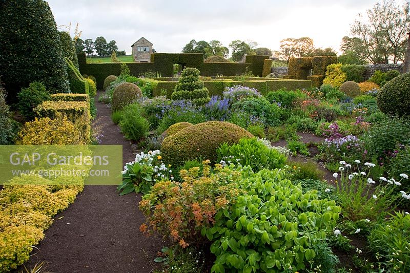 The Flower Garden features strong blocks of box and yew that frame cottage garden plants and flowers, including Euphorbia, Polemoniums and Geraniums - Herterton House, Hartington, Northumberland, UK