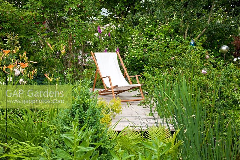 Deck chair on wooden deck in the margin zone of a garden pond with lush vegetation