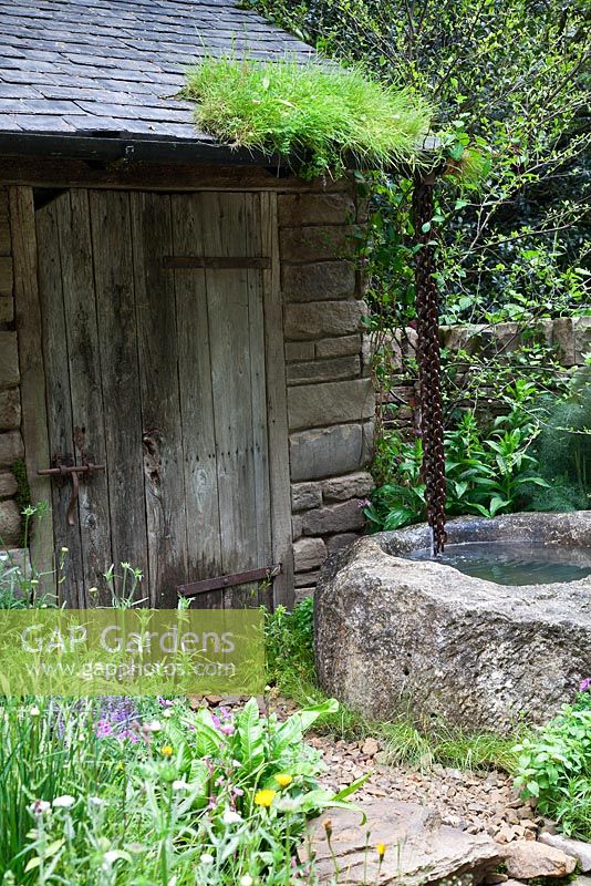 A stone water trough outside a garden building with naturalistic planting in the Naturally Dry - a William Wordsworth inspired garden at the RHS Chelsea Flower Show 2012