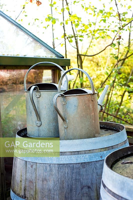 Two metal watering cans on wooden rainwater barrel