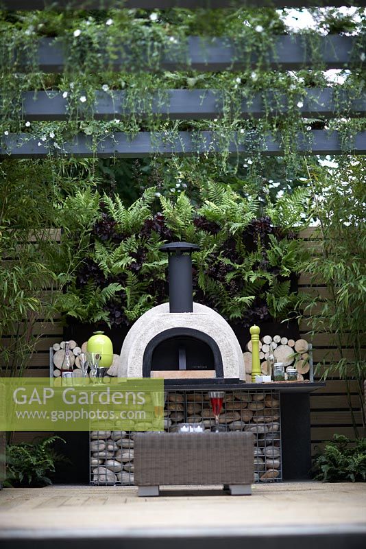 'Live Outdoors'. Hampton Court Flower Show 2012. Outdoor stove and seating area with vertical planting of ferns and dark heucheras.
