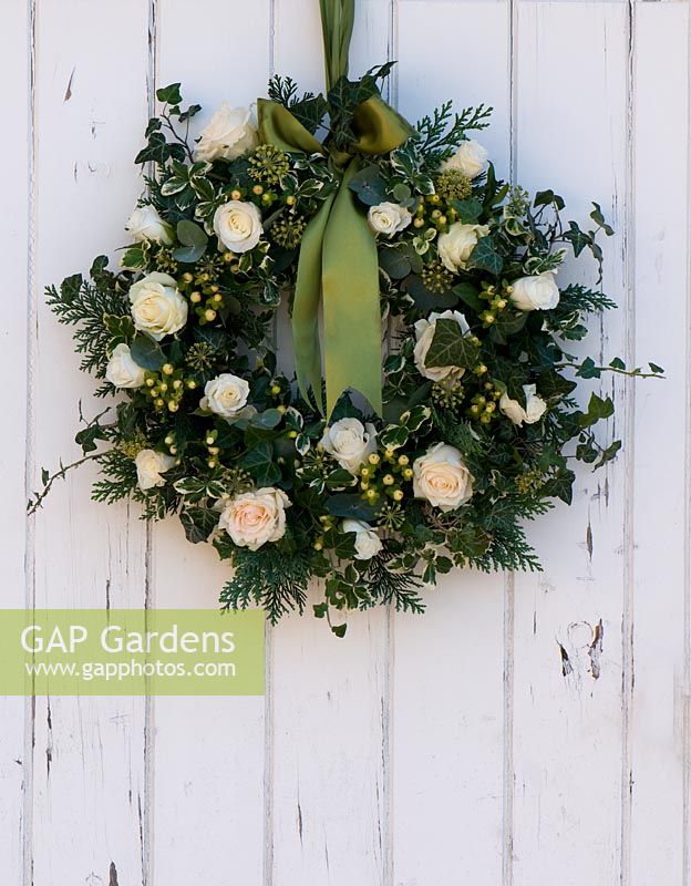 Christmas wreath hanging on white painted wooden door. Includes Rosa 'Artemis', Hypericum 'White Condor', Ivy and variegated Euonymus.