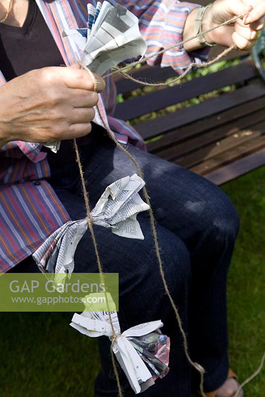Person making folded newspaper bird and butterfly scarers to hang over a vegetable bed