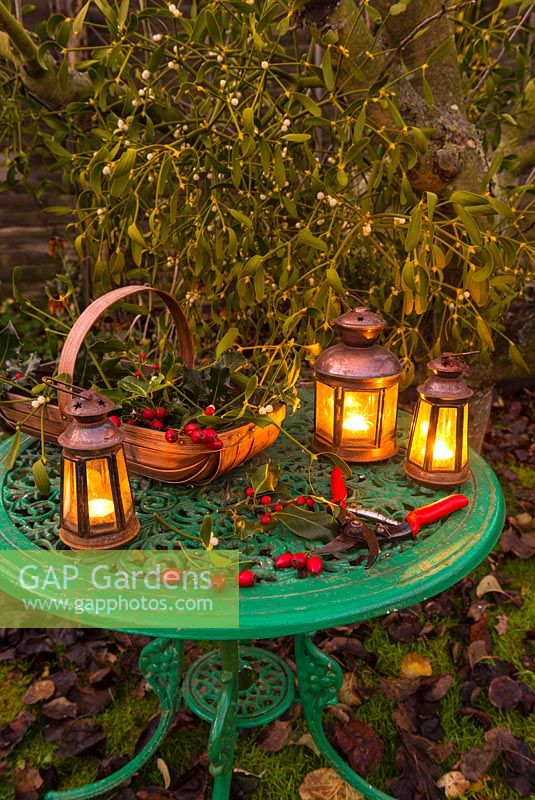 Garden table with Christmas lanterns and trug with mistletoe, rose hips, and holly