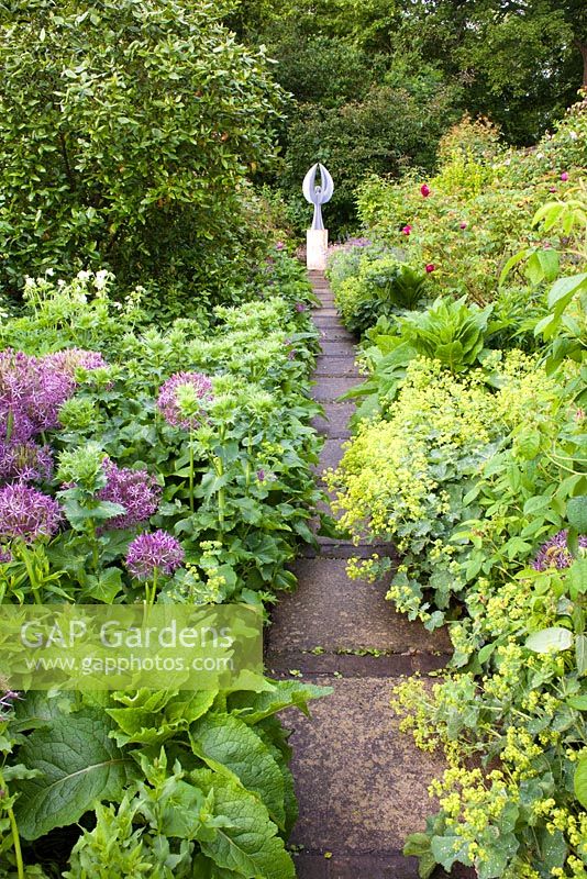 Summer borders and path leading to sculpture on a plinth in walled garden at Old Bladbean Stud. Planting icludes Alchemilla mollis, Allium, roses and many perennials.

