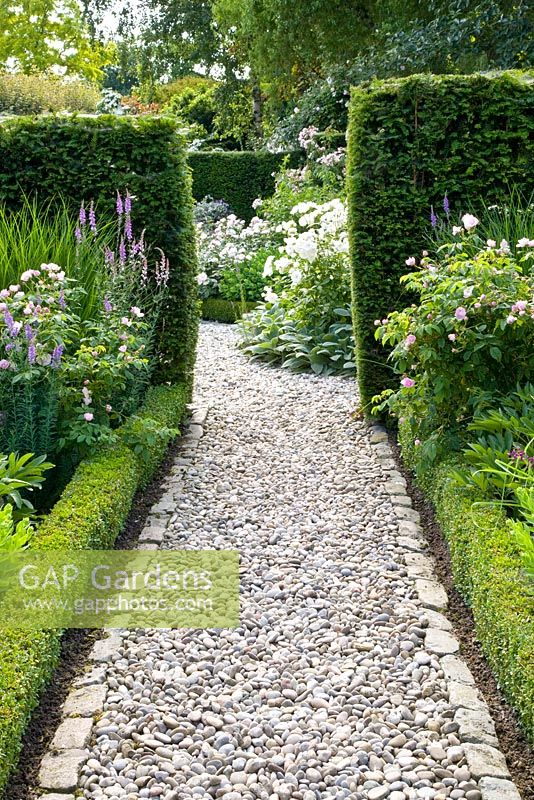 Pathway running through Summer borders with hedges separating garden rooms