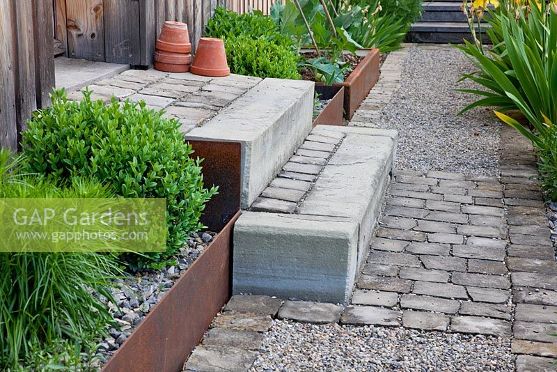 Corten steel edged plant troughs and steps made of concrete and granite, paving accentuates house entrance