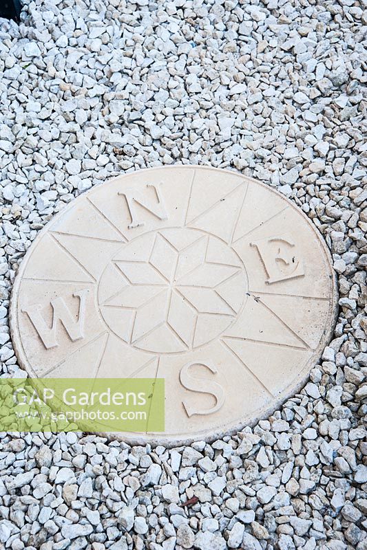 Circular compass stone embedded in gravel in front garden