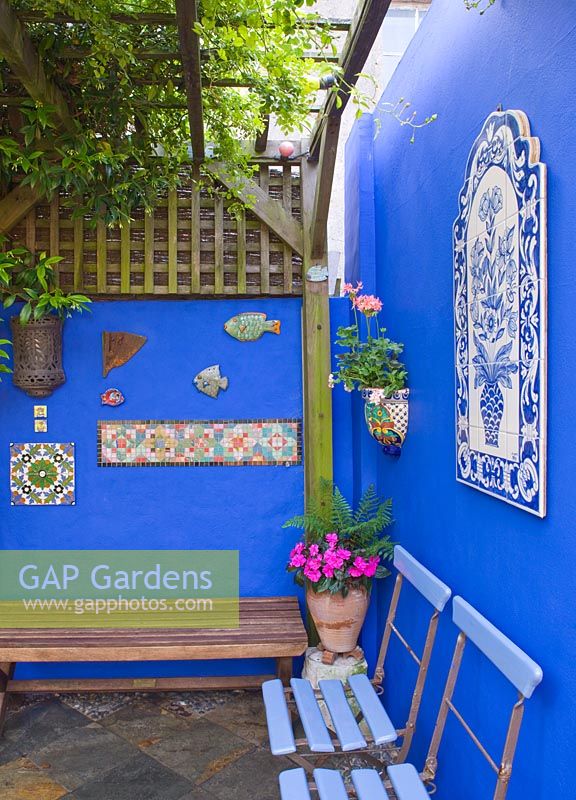 Courtyard with painted blue walls using powder pigment. Wooden benches and decorative tiles under pergola 