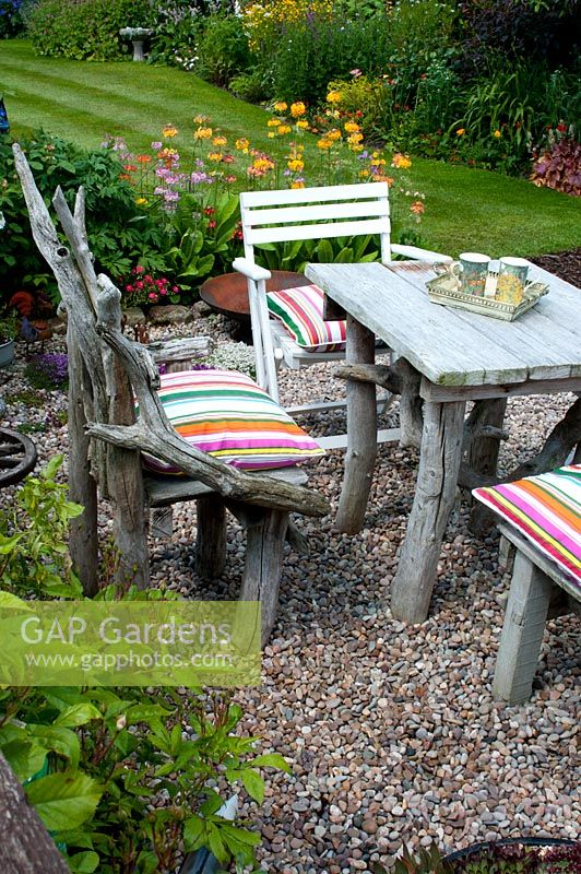 Chairs and square table made of drift wood on graveled corner of cottage garden 