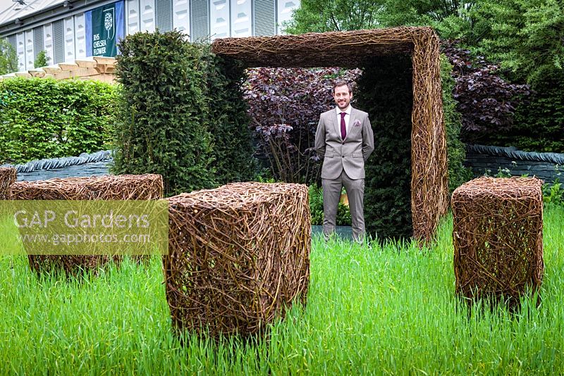 As Nature Intended Garden, Silver gilt medal winner, Chelsea Flower Show 2013. Jamie Dunstan standing between woven willow sculptures and yew hedging.